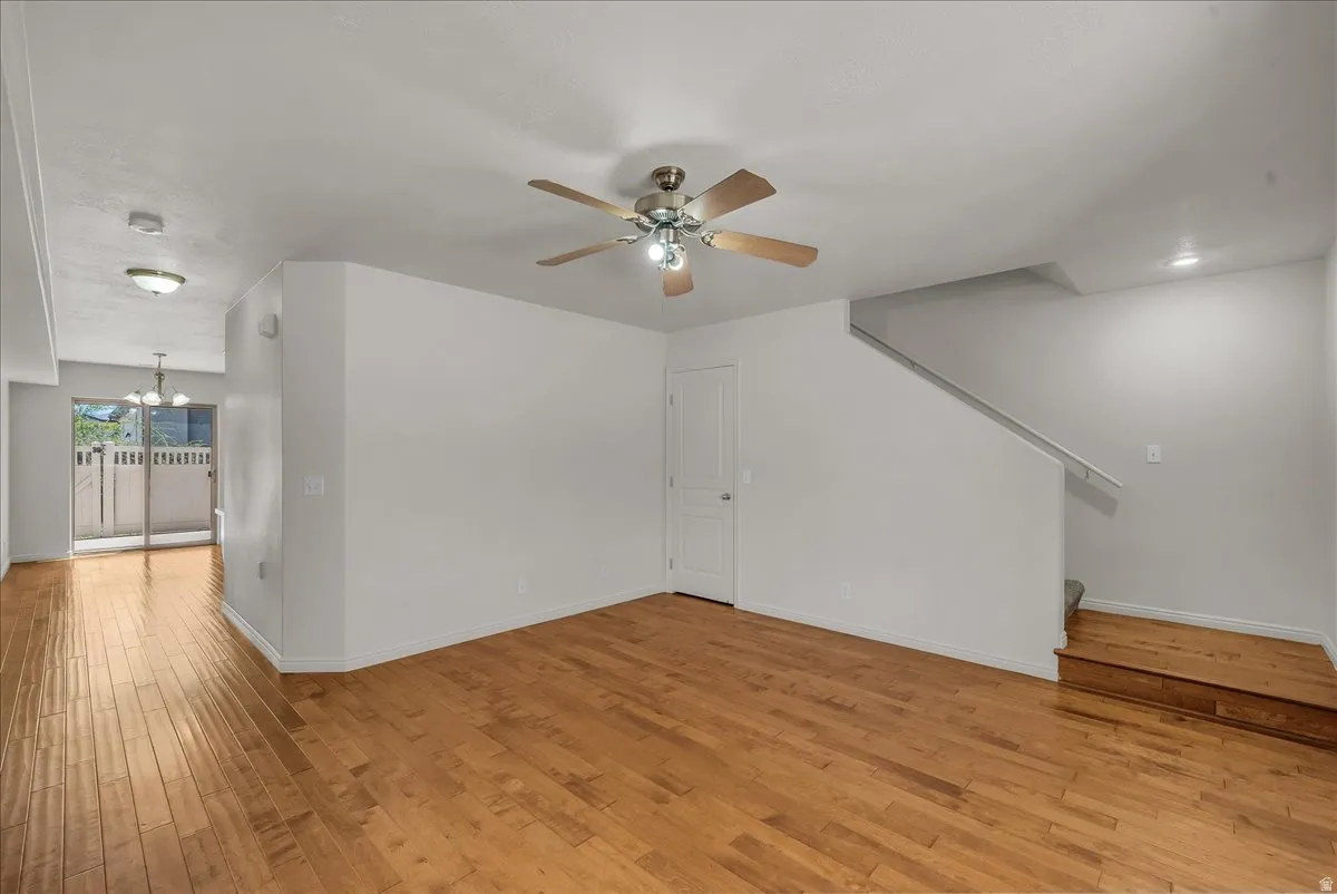 Bright, open living space filled with natural light, featuring wood-finish flooring, a ceiling fan, and a staircase with a crisp white railing.