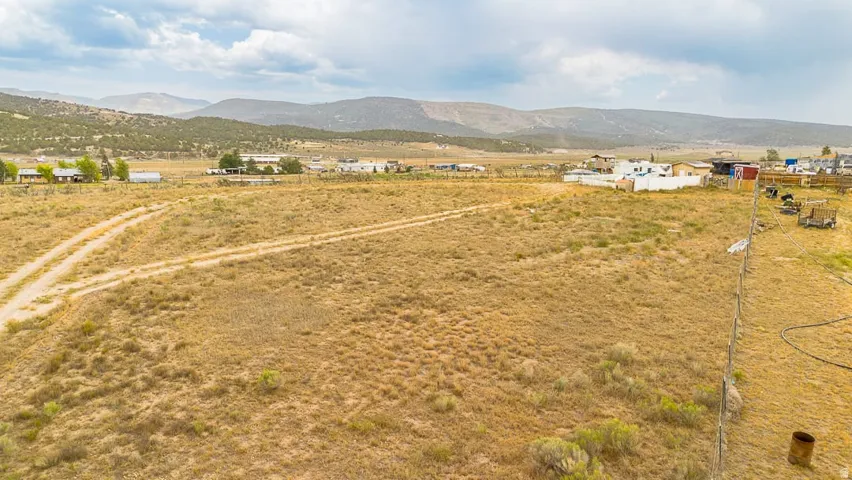 Expansive open land featuring natural desert vegetation, defined dirt tracks, a perimeter fence line, and distant mountain backdrops