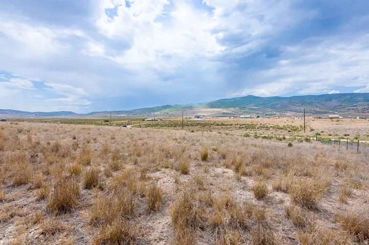 Expansive undeveloped land featuring natural grasses and distant mountain formations under a partially clouded sky