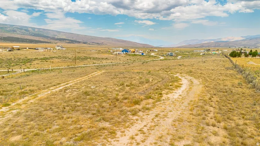 Expansive open land with a visible dirt road traversing the property, featuring distant mountains and a partially cloudy sky