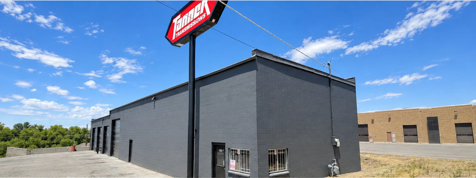 Commercial building featuring a dark gray painted brick exterior, multiple garage doors, and a prominent freestanding business sign