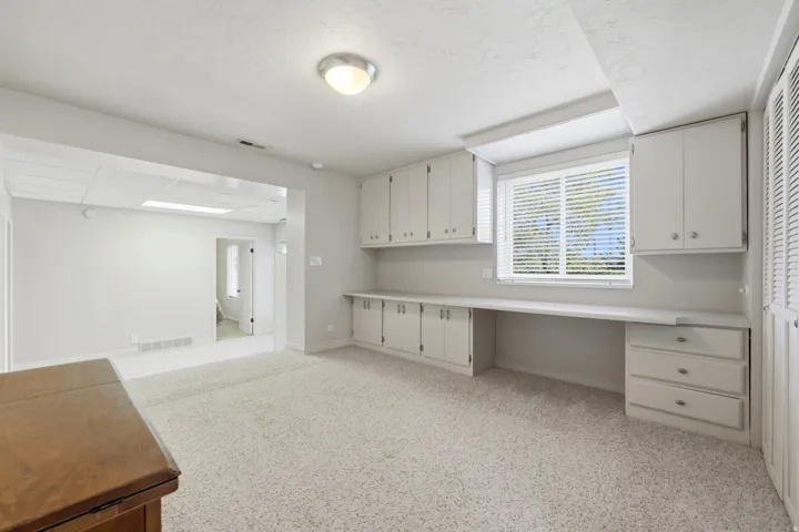 Dedicated workspace featuring extensive built-in cabinetry, an integrated desk, and a window with horizontal blinds