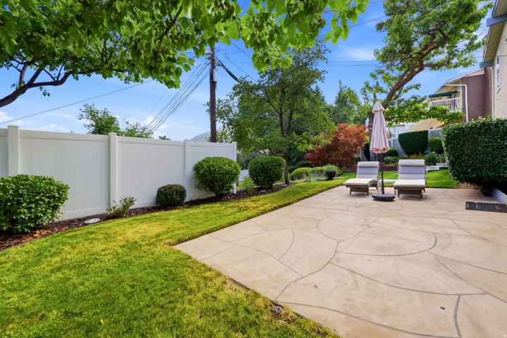 Expansive backyard featuring a patterned concrete patio, manicured lawn, and a privacy fence