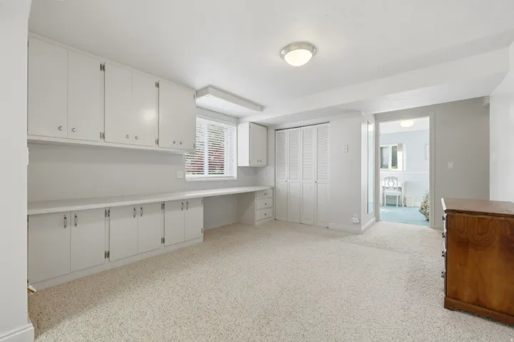 Integrated desk space featuring extensive built-in white cabinetry, window with blinds, and white bi-fold closet doors