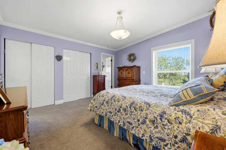 Bedroom featuring neutral carpet flooring, white crown molding, a large window with horizontal blinds, and a semi-flush mount ceiling light