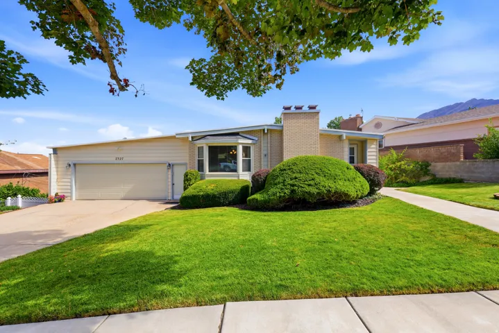 Ranch-style residence featuring a prominent bay window, attached garage, and a brick chimney