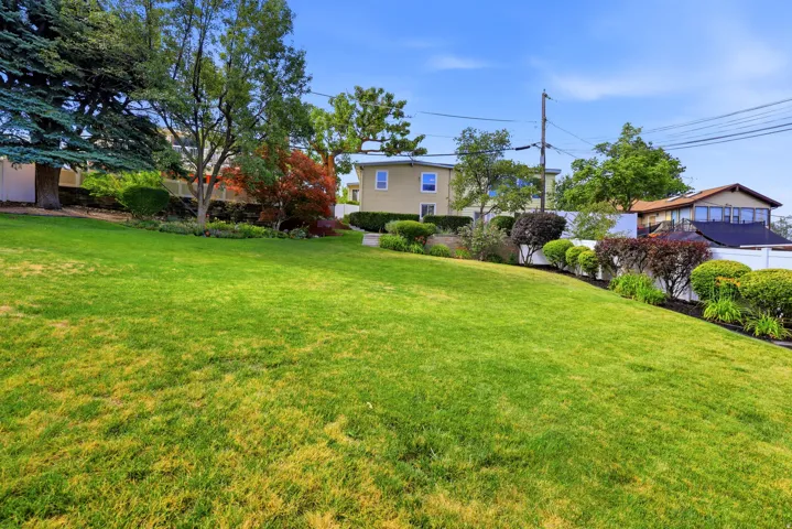 Expansive graded lawn featuring mature trees and established shrubbery, framed by a white privacy fence