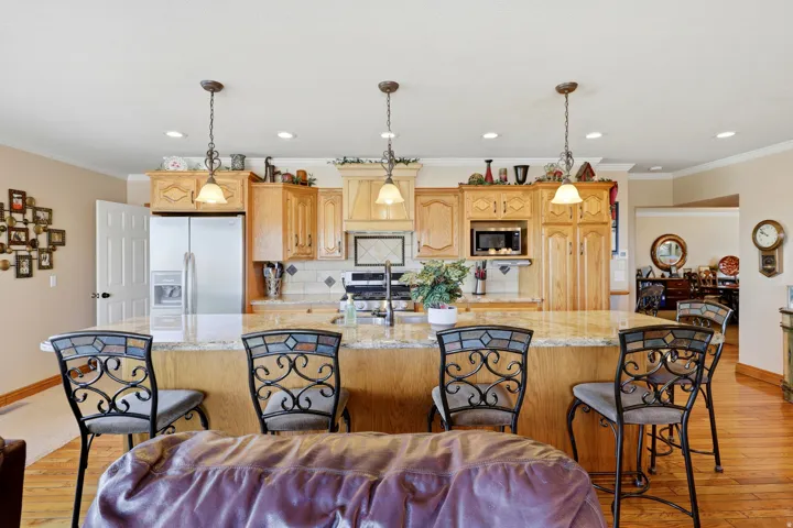 Expansive kitchen island featuring a light-toned countertop, integrated double sink, stainless steel appliances, wood-finish cabinetry, and decorative pendant lighting