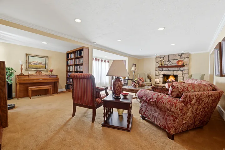 Spacious living area featuring a stone fireplace with a wood mantle, recessed lighting, and crown molding