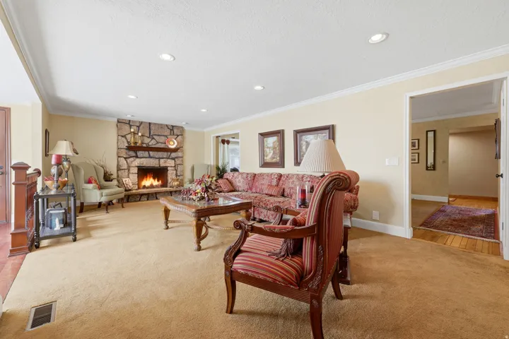 Living area featuring a stone fireplace with a wood mantle, recessed lighting, crown molding, and carpeting