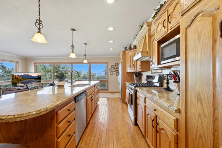 Kitchen featuring wood-finish cabinetry, granite-style countertops, stainless steel appliances, a large center island with integrated sink, and wood-finish flooring
