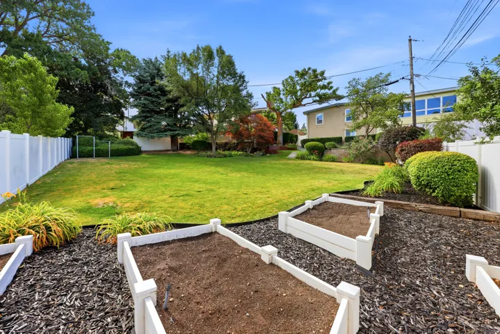 Spacious backyard featuring a manicured lawn, white vinyl fencing, and multiple raised garden beds