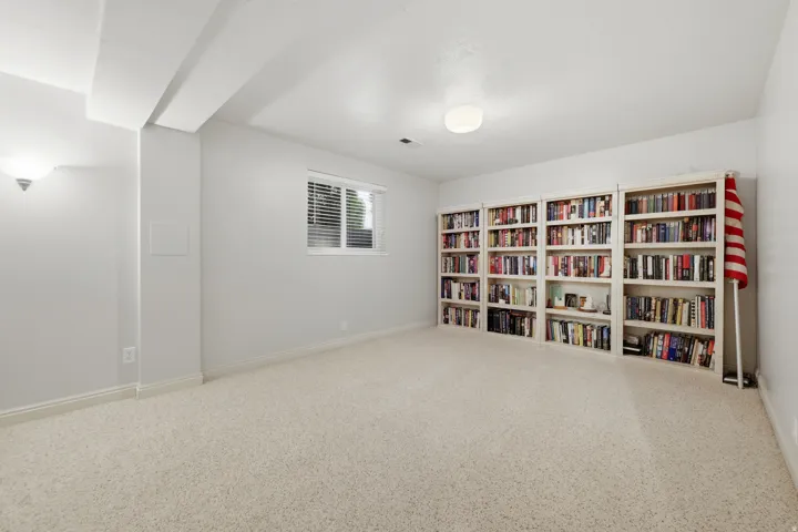 Spacious room featuring extensive built-in shelving, plush carpeting, a single window with blinds, and white painted walls with trim