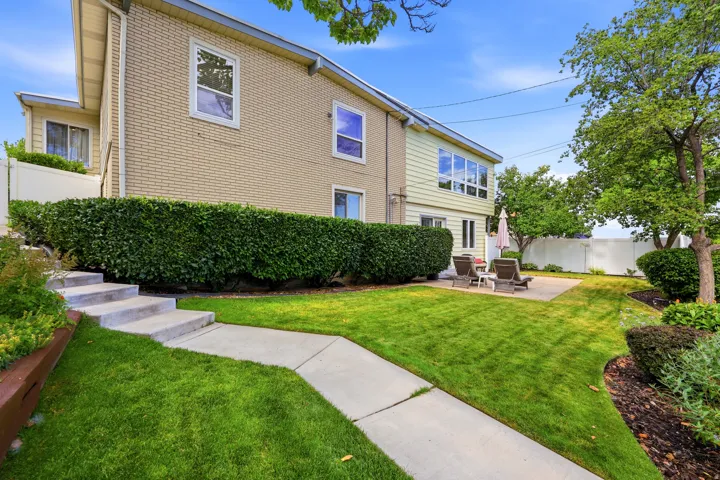 Expansive backyard featuring a lush lawn, mature trees, concrete patio, and garden beds with integrated landscaping