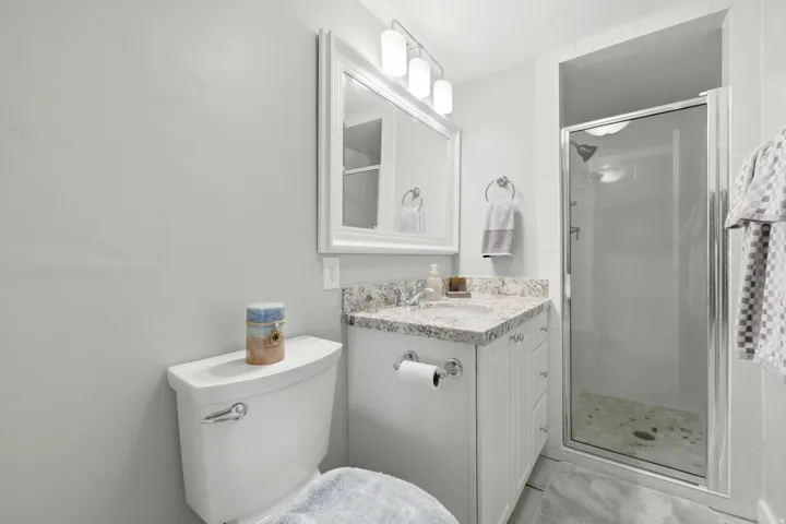 Modern bathroom featuring a white vanity with a granite countertop, a framed mirror, and a three-light fixture