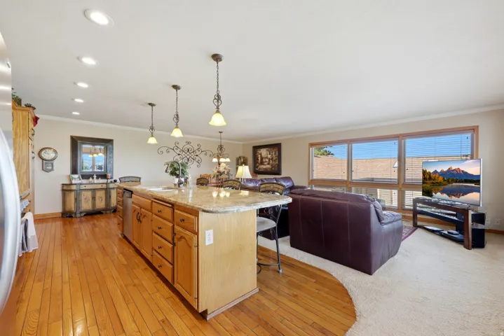 Open-concept living area featuring a kitchen island with pendant lighting, wood-finish flooring, a wall of windows, recessed ceiling lights, and two distinct floor coverings