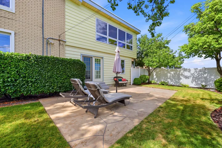 Rear exterior featuring a stamped concrete patio, manicured lawn, and mature privacy hedging