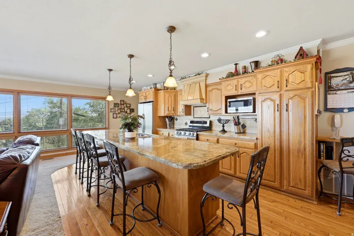 Open-concept kitchen featuring extensive wood cabinetry, a large center island with a natural stone countertop, pendant lighting, and stainless steel appliances