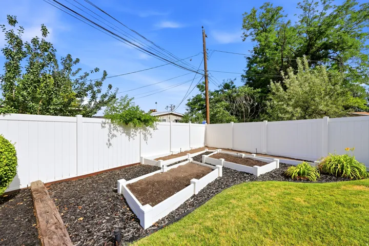 Manicured backyard featuring a white privacy fence, raised garden beds, a vibrant green lawn, and mature landscaping