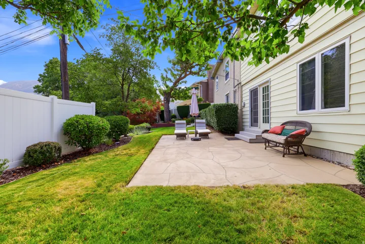 Spacious backyard featuring a stamped concrete patio, manicured lawn, white privacy fencing, mature landscaping, and double French doors providing direct outdoor access