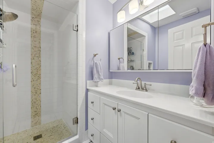 Bathroom featuring a glass-enclosed shower with mosaic tile accents, white vanity with integrated sink, chrome faucet, and mirrored medicine cabinet