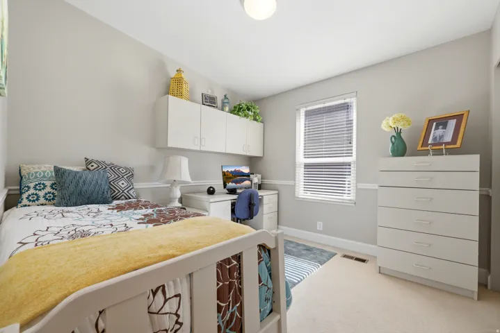 Carpeted room featuring a window with blinds, baseboards, and a built-in desk with overhead cabinetry