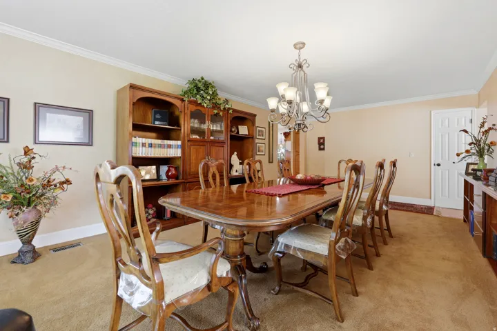 Formal dining area featuring a decorative chandelier, crown molding, built-in wooden cabinetry, and carpeting