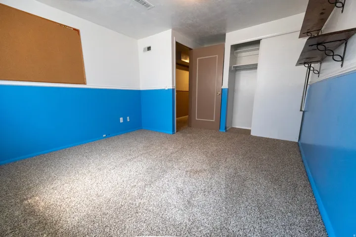 Carpeted room with a two-tone wall treatment, featuring a cork board and built-in shelving