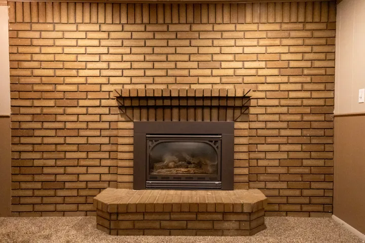 Brick fireplace featuring a hearth, dark-toned insert, and mantel shelf