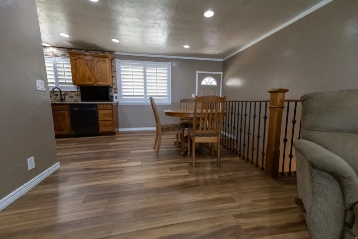 Open-concept living space featuring wood-finish flooring, recessed lighting, and a kitchen area with wood cabinetry and a tile backsplash