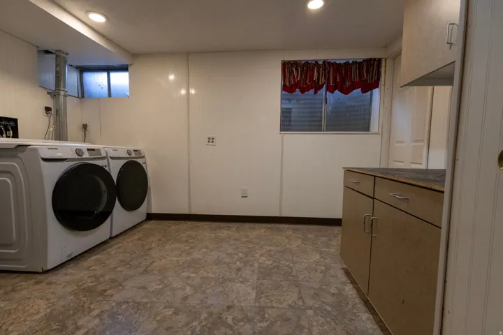 Laundry area featuring white paneling, tile-finish flooring, a built-in window, and integrated cabinetry with a countertop surface