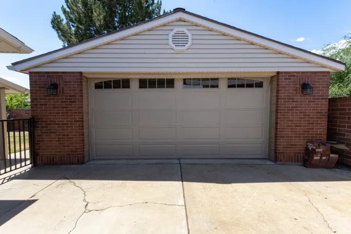 Two-car garage featuring a tan overhead door with arched window inserts, brick-clad exterior walls, and light-colored siding on the gable