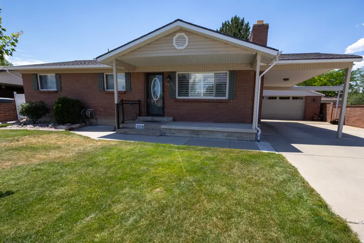 Brick facade residence featuring a covered front porch, an oval-paneled front door, a connected carport, an attached garage, and a concrete driveway