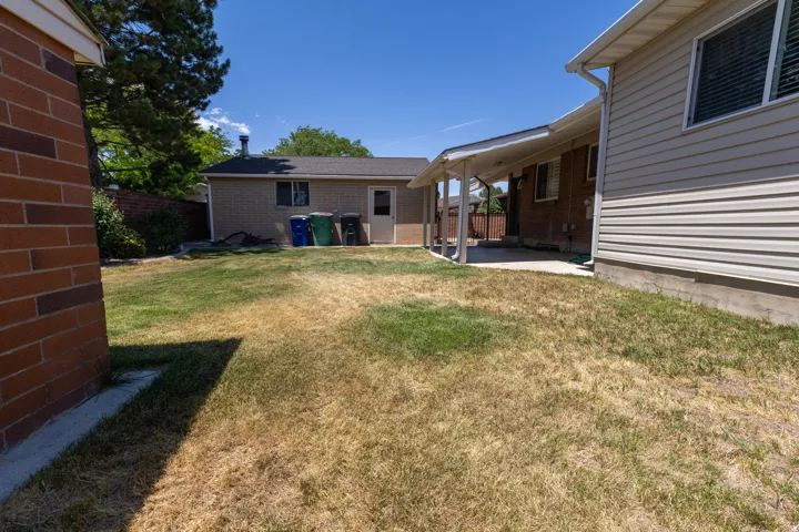 Expansive backyard featuring a covered patio, brick exterior, and a detached building