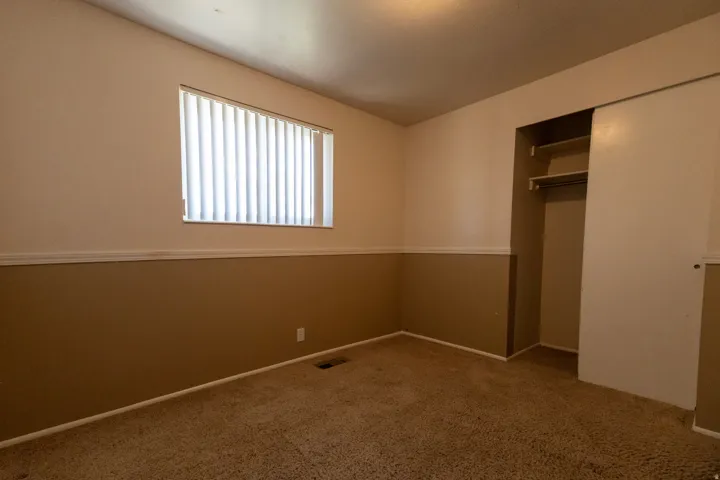 Bedroom featuring carpeting, a window with vertical blinds, a built-in closet with sliding doors, and bi-color painted walls