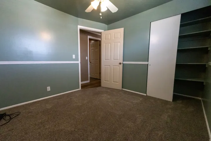 Spacious room featuring neutral carpet flooring, two-tone painted walls with chair rail molding, and a ceiling fan with integrated lighting