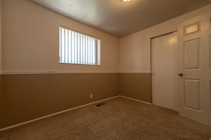 Carpeted interior space featuring a window with vertical blinds, two-tone wall paint with a chair rail, a white sliding closet door, and a paneled entry door with a chrome knob
