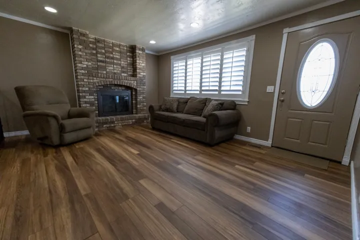 Spacious room featuring wood-finish flooring, a brick fireplace with an arched opening, and recessed ceiling lights