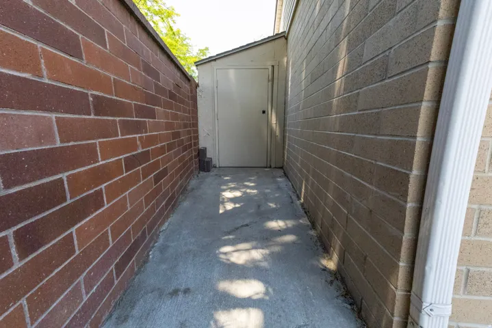 Concrete pathway bordered by a multi-tone brick privacy wall and a tan brick building