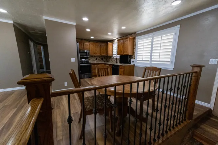 Open-concept kitchen and dining area featuring wood-finish flooring, recessed lighting, and a kitchen with warm-toned cabinetry, stainless steel appliances, and a tiled backsplash