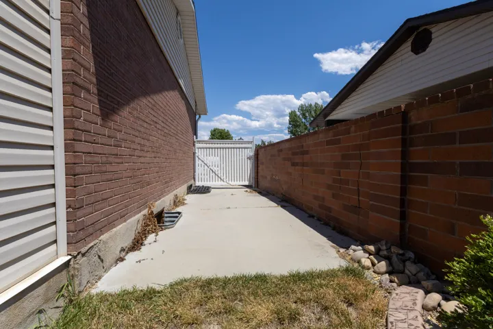 Concrete pathway featuring a white picket style gate, red brick wall, and beige siding
