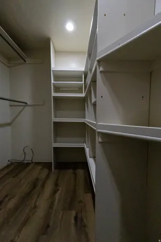 Walk-in closet featuring built-in shelving, hanging rods, recessed ceiling lighting, and wood-finish flooring
