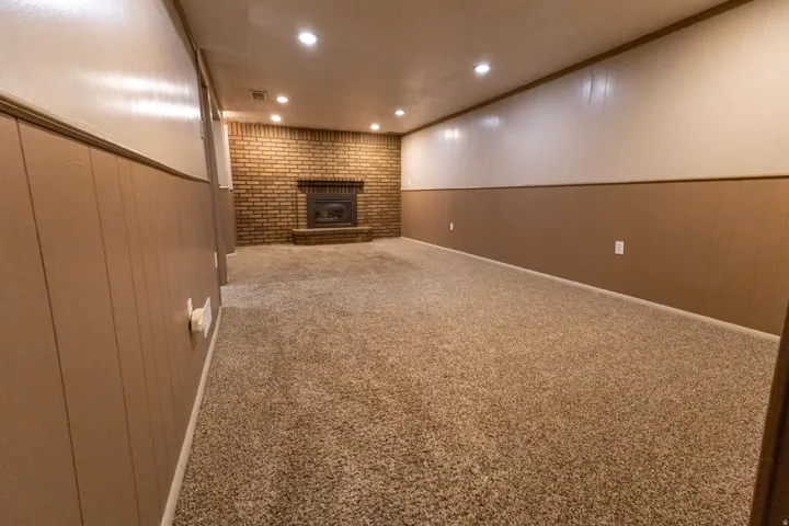 Spacious room featuring plush carpeting, a brick fireplace with a hearth, recessed lighting, and wainscoting with a two-tone wall finish