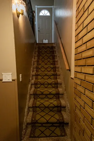 Staircase featuring a patterned carpet runner, wood handrail, and a brick-look accent wall