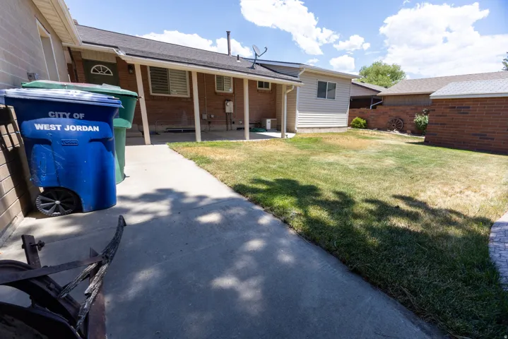 Rear exterior featuring a covered patio, brick and siding finishes, a partial concrete pathway, and a grassy area