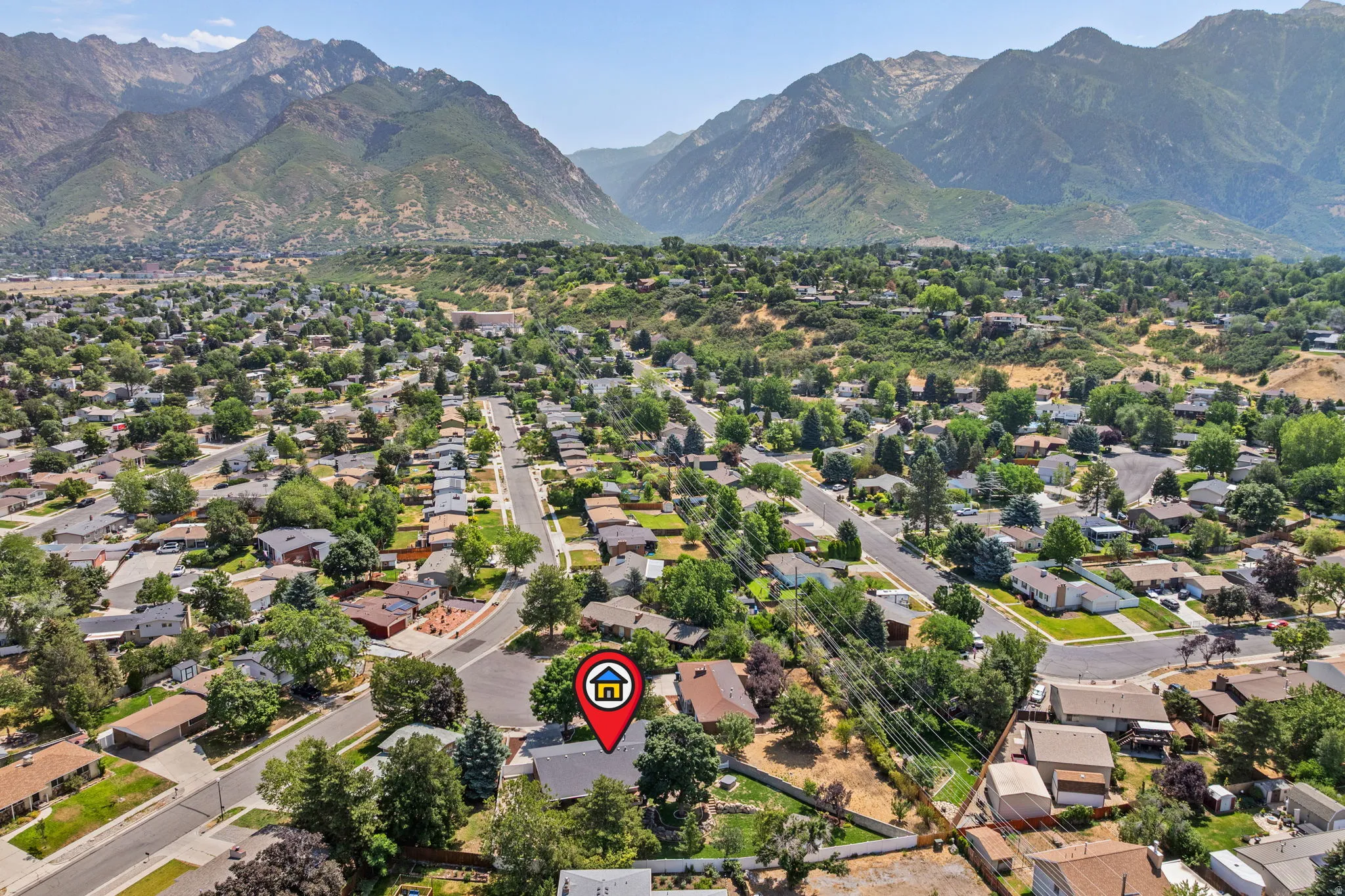 Aerial perspective showcasing a residential neighborhood with established homes, mature trees, and mountainous terrain in the background