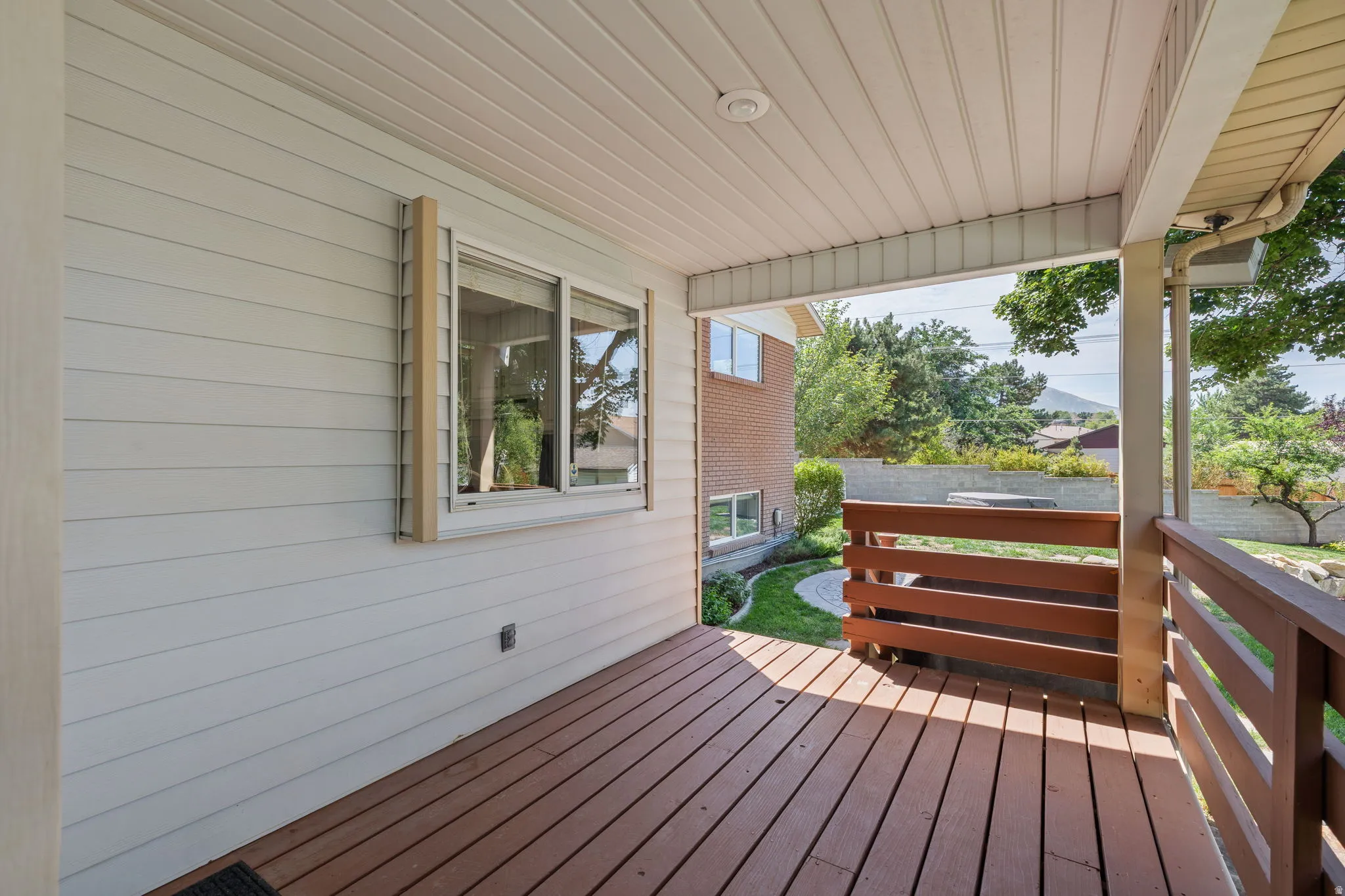 Covered porch featuring wood-finish decking, horizontal wood railings, and a white paneled ceiling