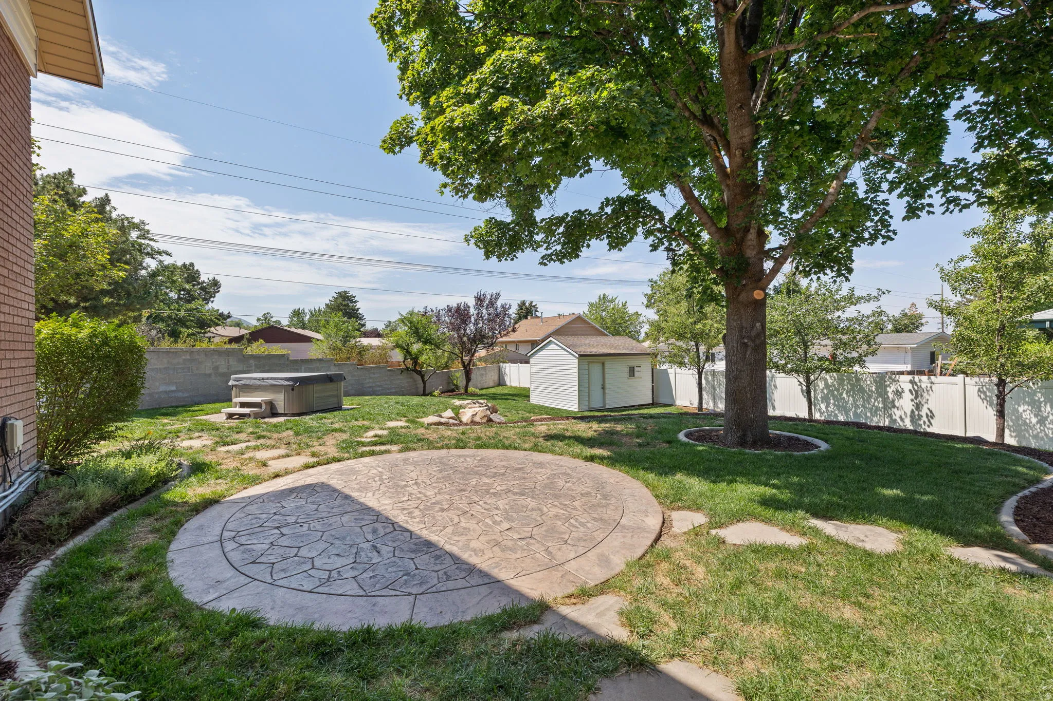 Spacious backyard featuring a stamped concrete patio, hot tub, mature trees, and a storage shed