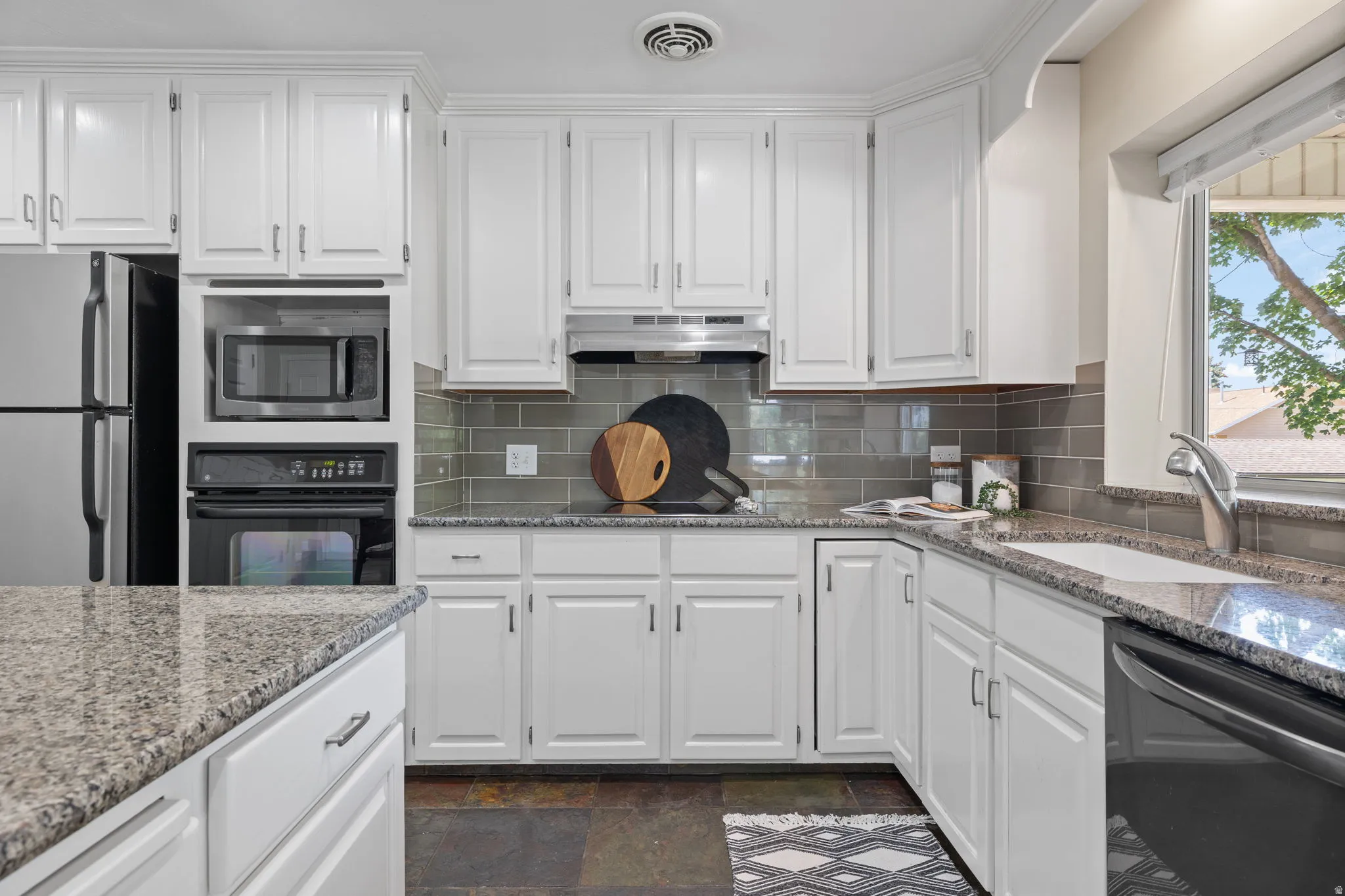 Kitchen featuring extensive white cabinetry, granite countertops, subway tile backsplash, built-in microwave, and stainless steel appliances
