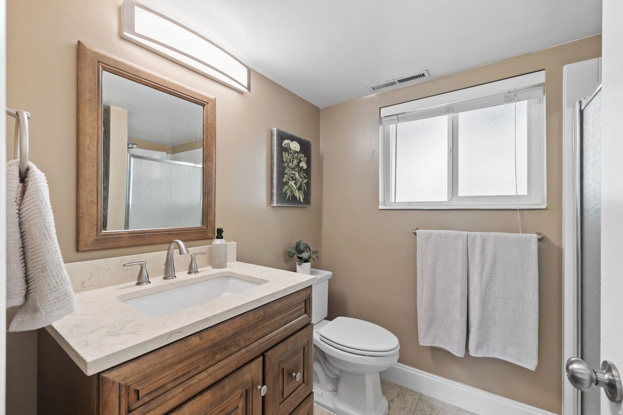 Bathroom featuring a wood-finish vanity with a light-toned countertop and an undermount sink